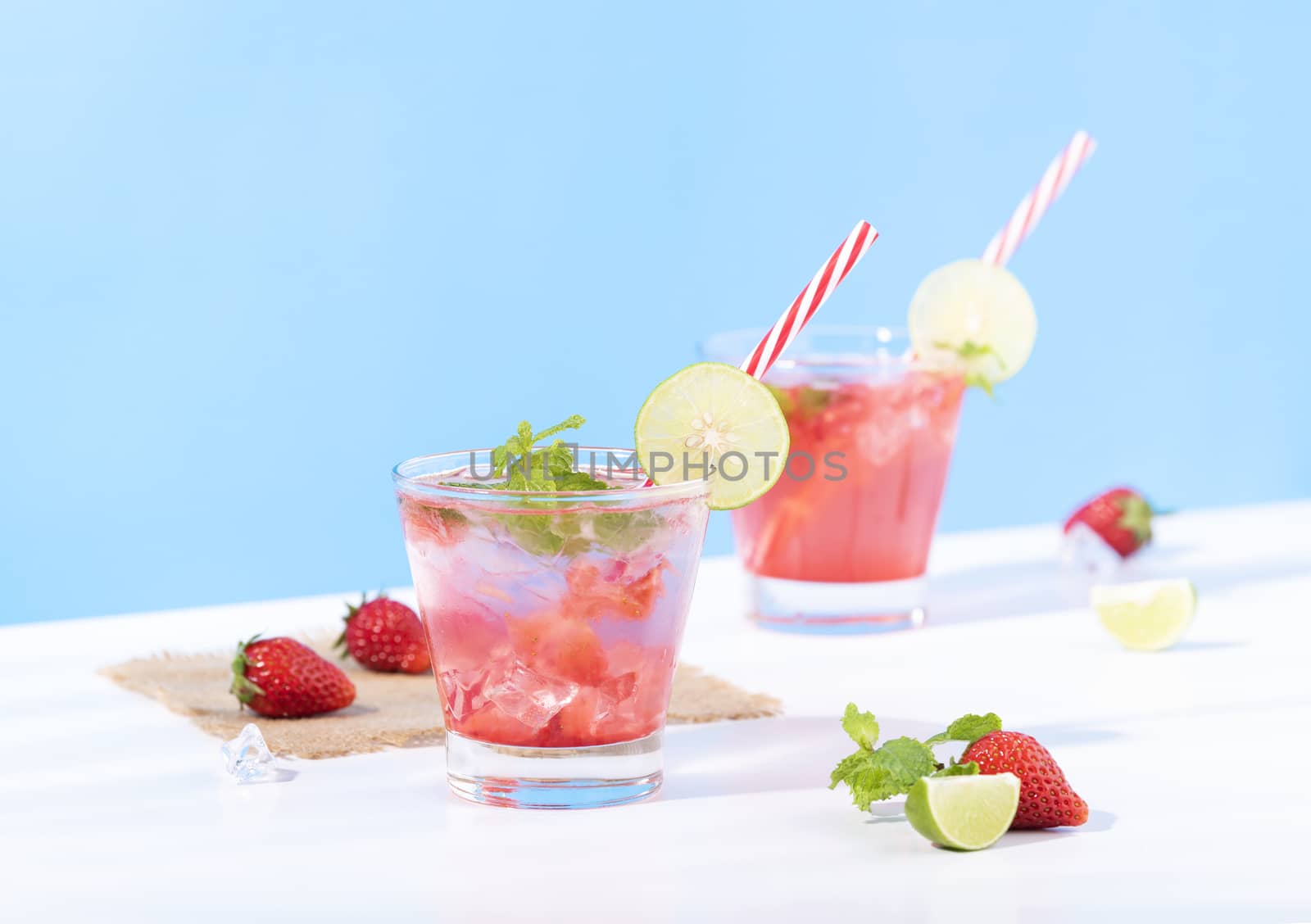 iced strawberry punch cocktail in glass with lemon on blue background. summer drink.