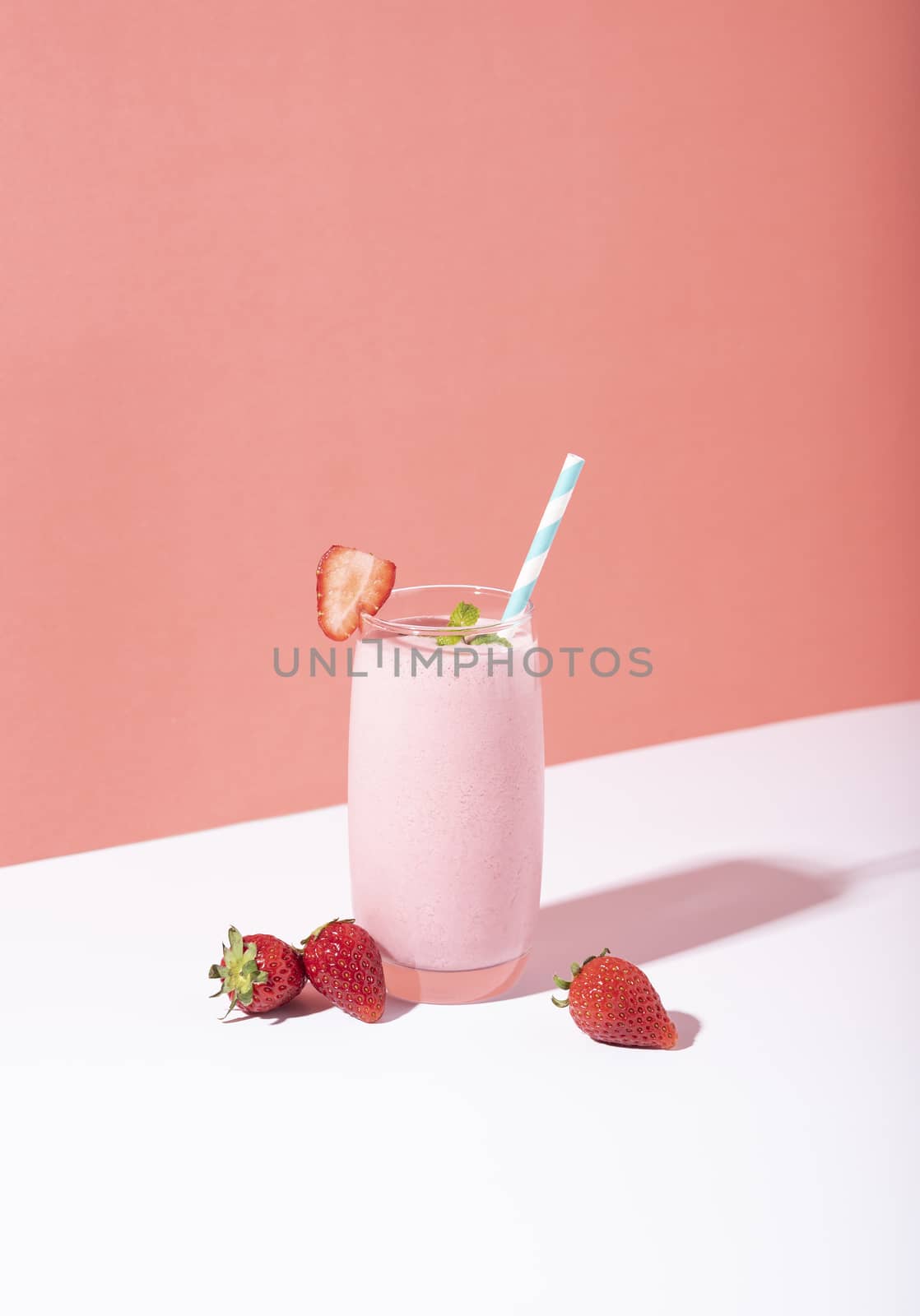 Strawberry smoothie in glass with straw and scattered berries on pink background. by barameeyay