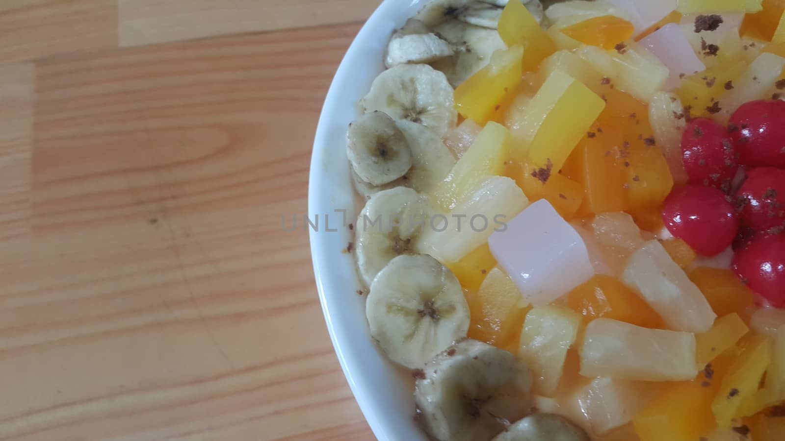 Creamy tasty sweet fruit trifle over custard with banana slices layered on surface on wooden floor. A top view of home made fruit trifle, a products for dessert after meal.