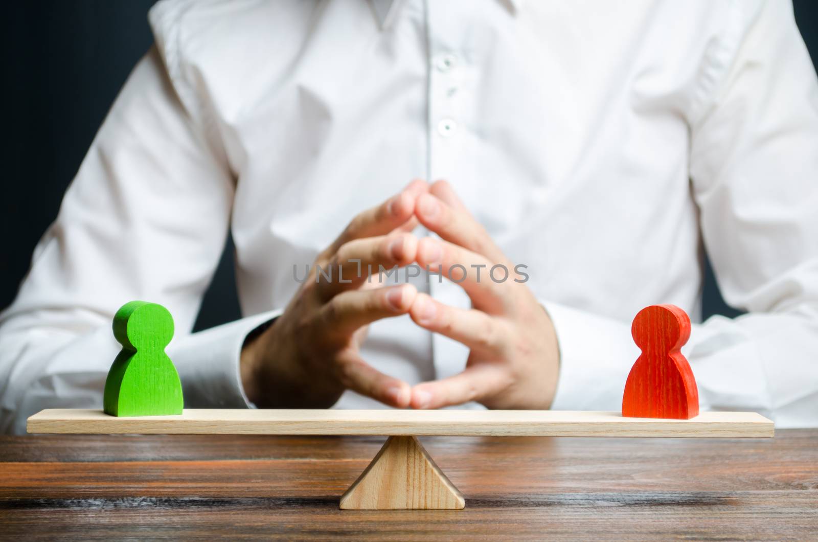 A man with hands in the lock and looks at the rival red and green figures on a scales. The concept of conflict resolution and the search for a compromise in the dispute. Weighted decision