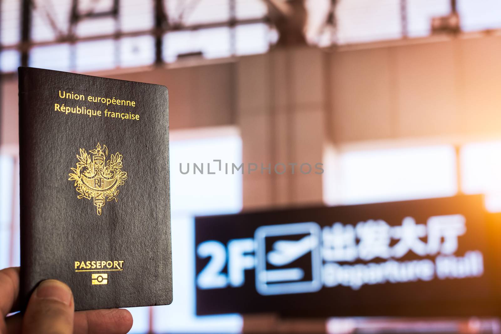 Hand holding a french passport in a chinese airport departure hall with the sun passing through the windows