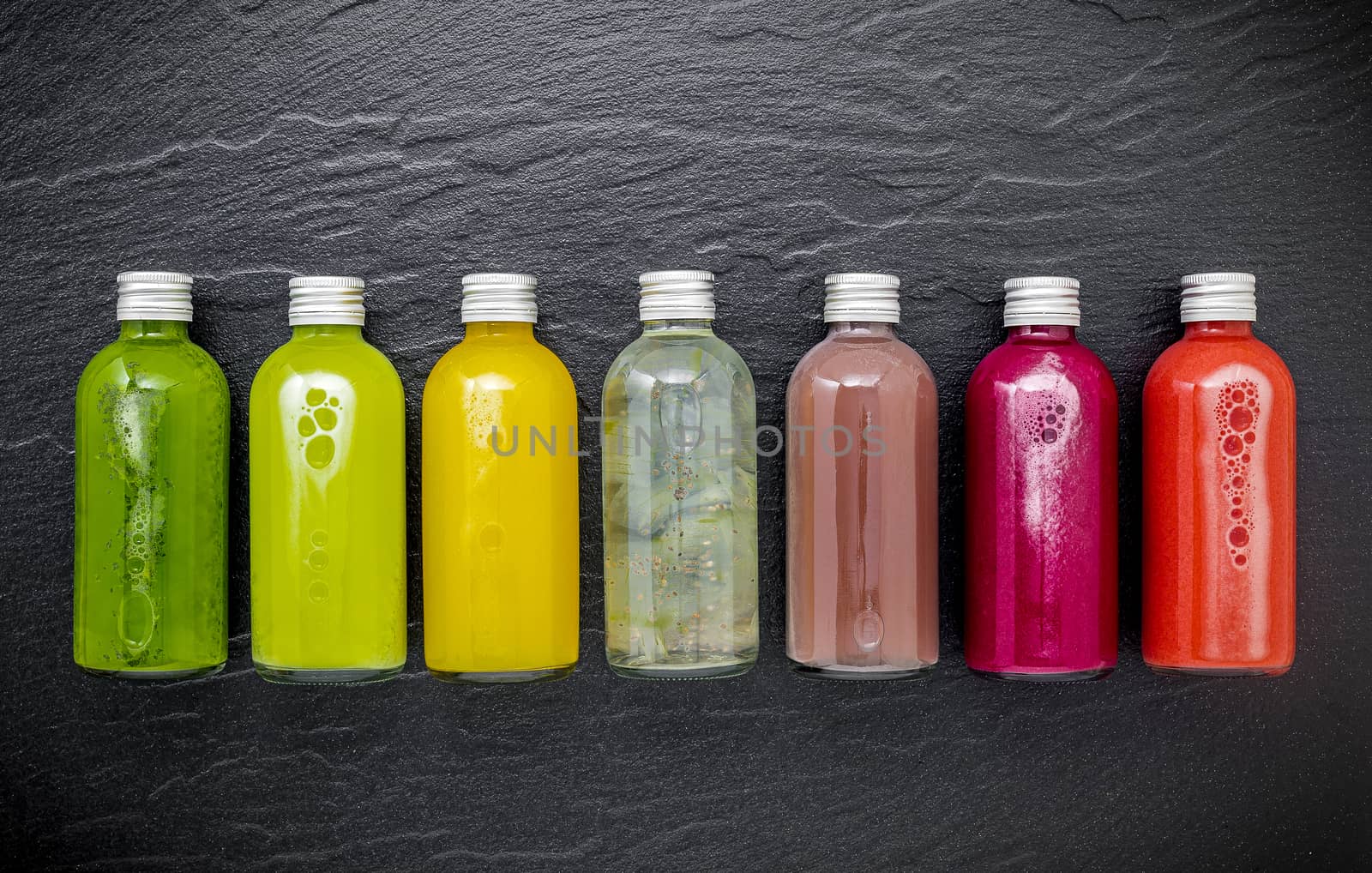 Colourful healthy smoothies and juices in bottles on dark stone background with copy space.