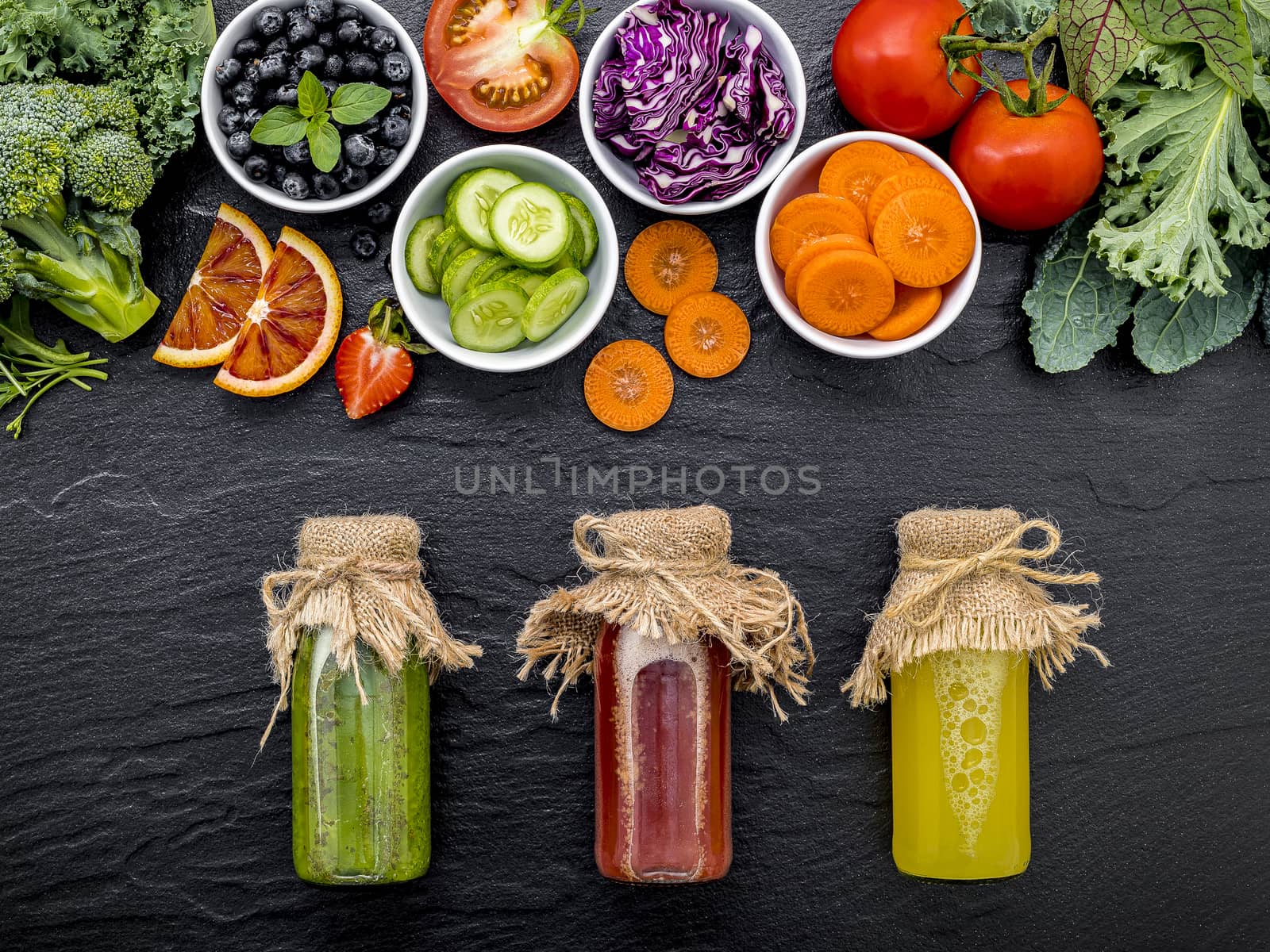 Colourful healthy smoothies and juices in bottles with fresh tropical fruit and superfoods on dark stone background with copy space.