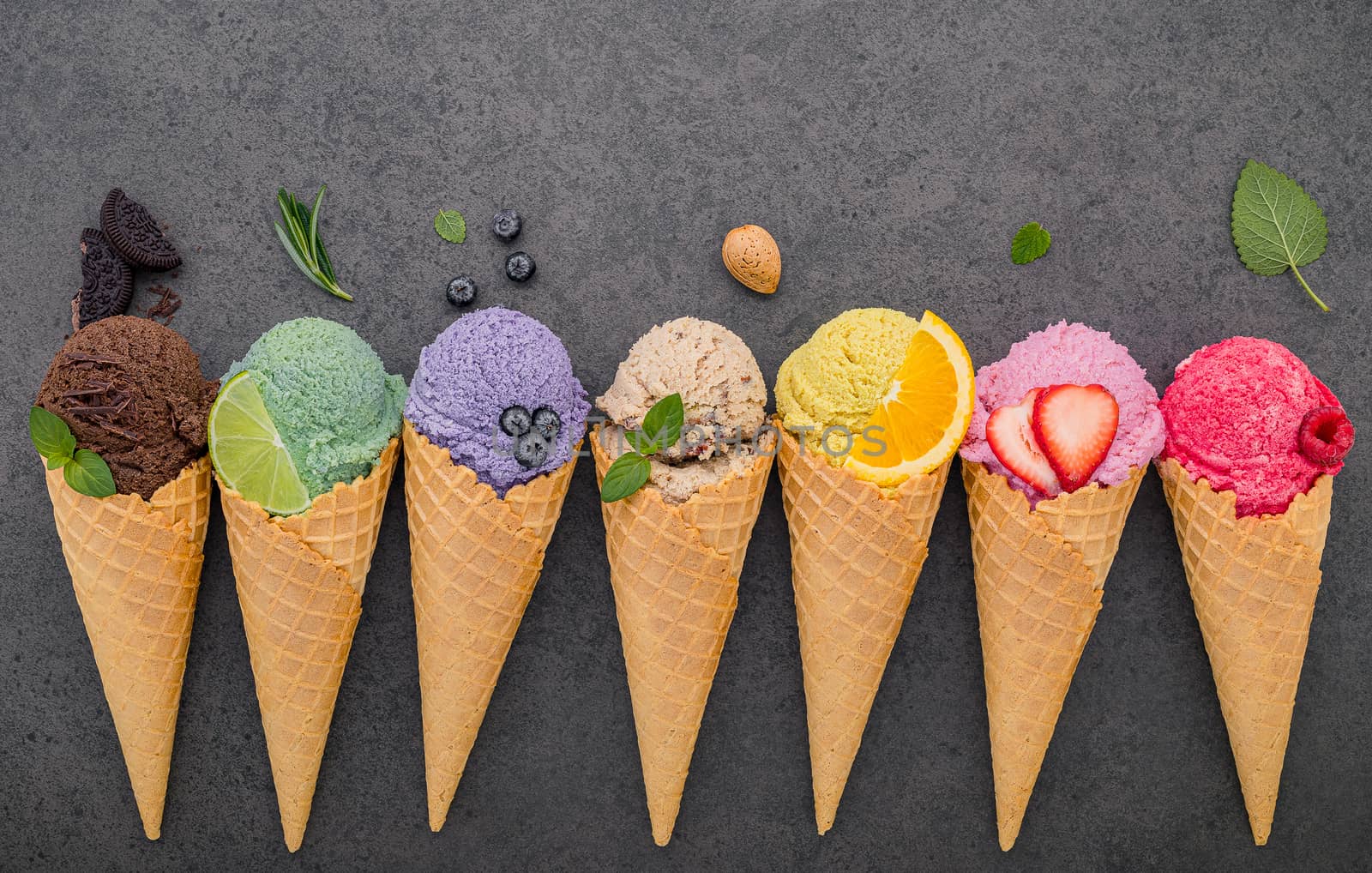 Various of ice cream flavor in cones blueberry ,lime ,pistachio ,almond ,orange ,chocolate ,vanilla and coffee set up on dark stone background . Summer and Sweet menu concept.