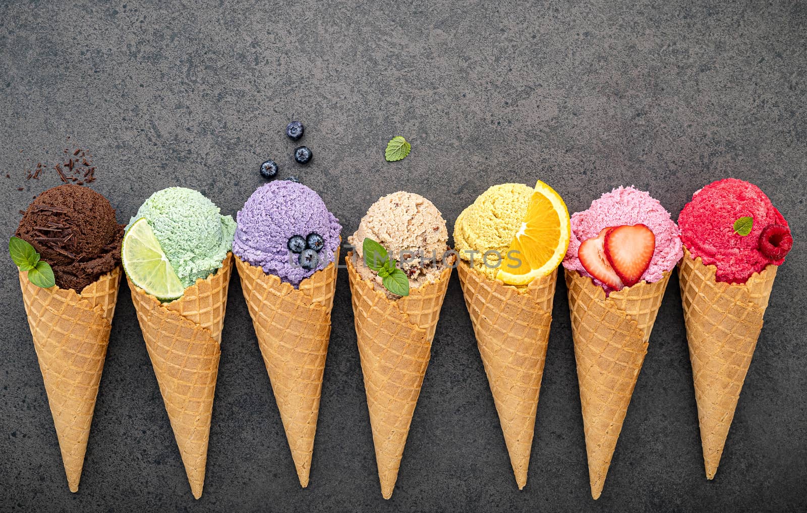 Various of ice cream flavor in cones blueberry ,lime ,pistachio ,almond ,orange ,chocolate ,vanilla and coffee set up on dark stone background . Summer and Sweet menu concept.