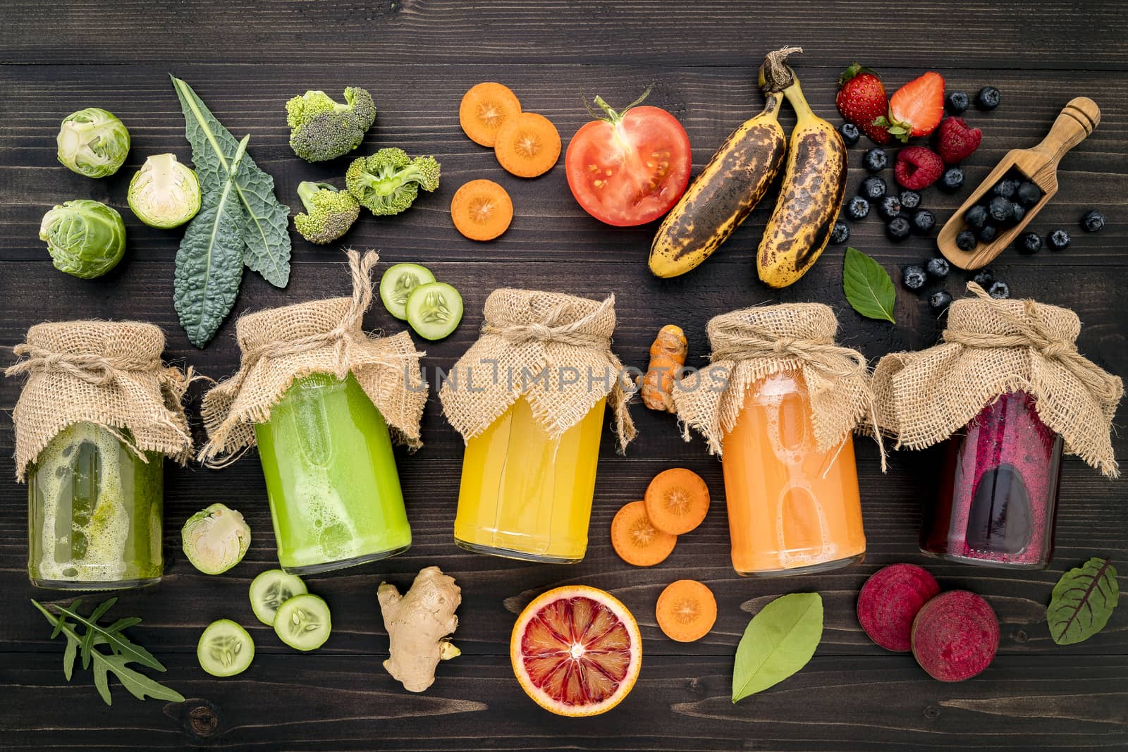 Colourful healthy smoothies and juices in bottles with fresh tropical fruit and superfoods on wooden background.