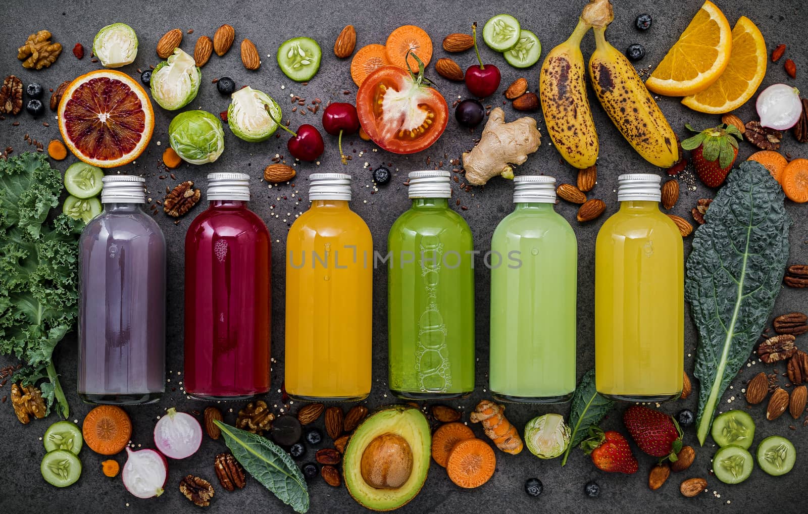 Colourful healthy smoothies and juices in bottles with fresh tropical fruit and superfoods on dark stone background with copy space.