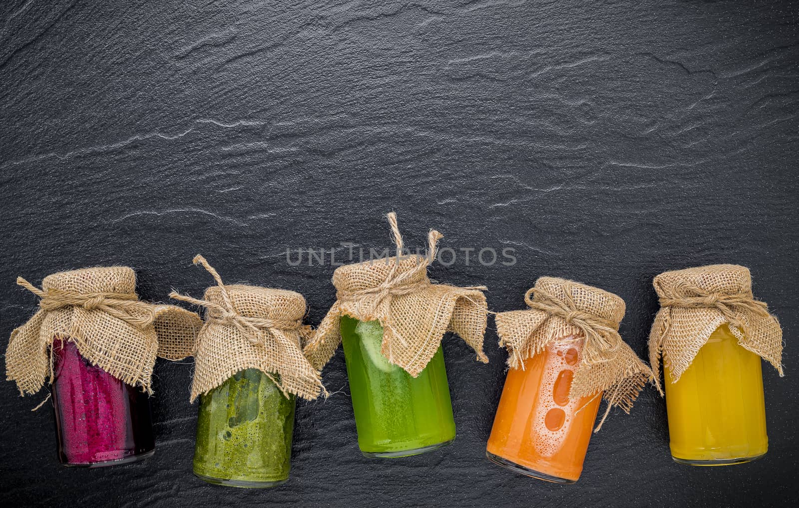 Colourful healthy smoothies and juices in bottles on dark stone background with copy space.