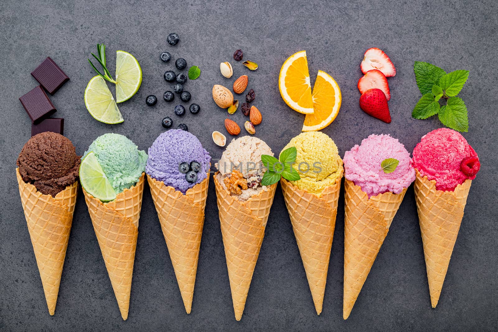 Various of ice cream flavor in cones blueberry ,lime ,pistachio ,almond ,orange ,chocolate ,vanilla and coffee set up on dark stone background . Summer and Sweet menu concept.