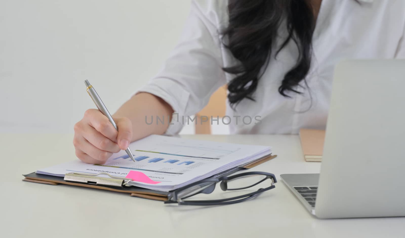 Close-up of Girl holding a pen in hand pointing at the graph and laptop on the desk in modern office.