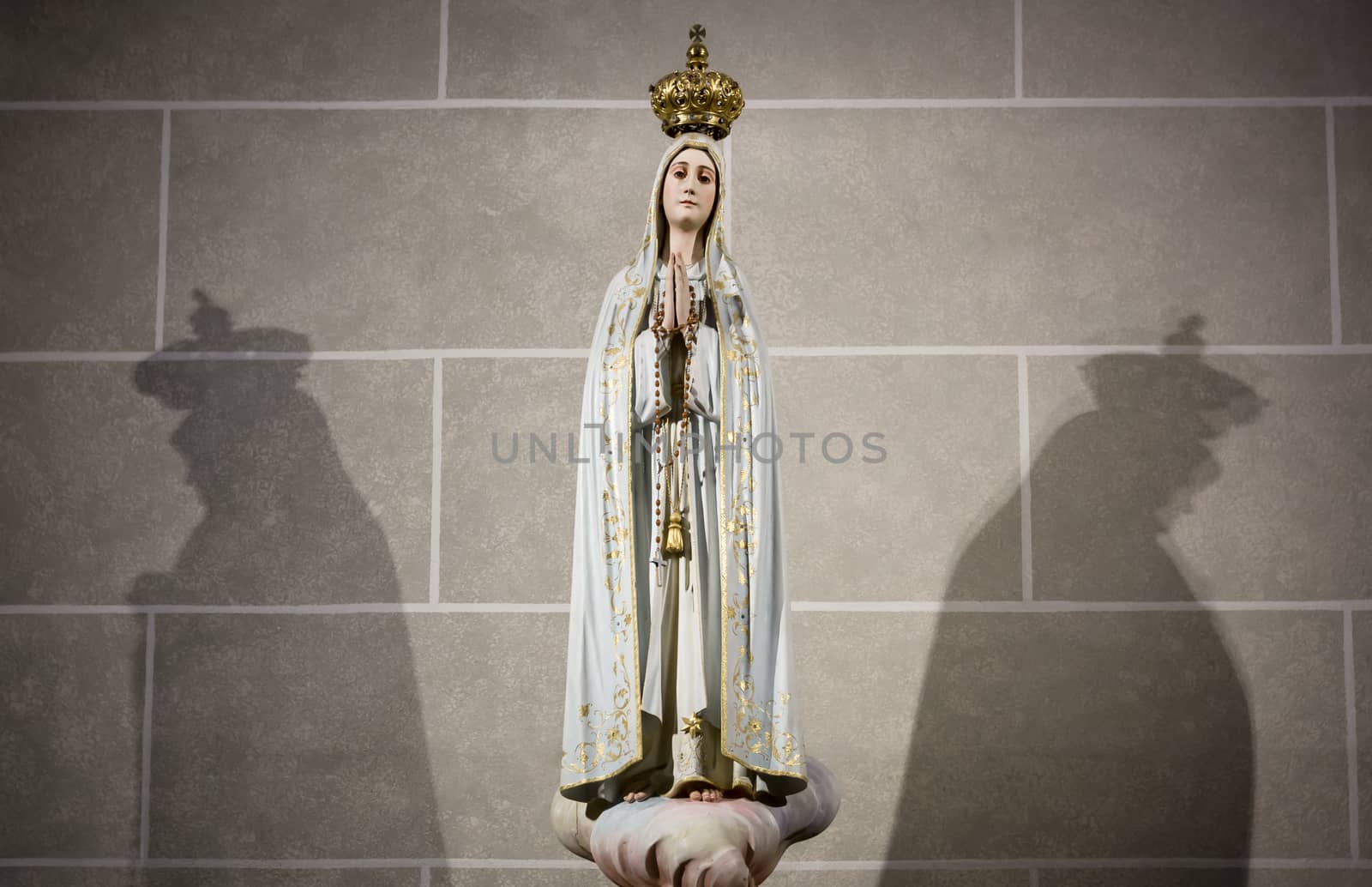 Staue of Virgin Mary with double shadow against a church's wall.