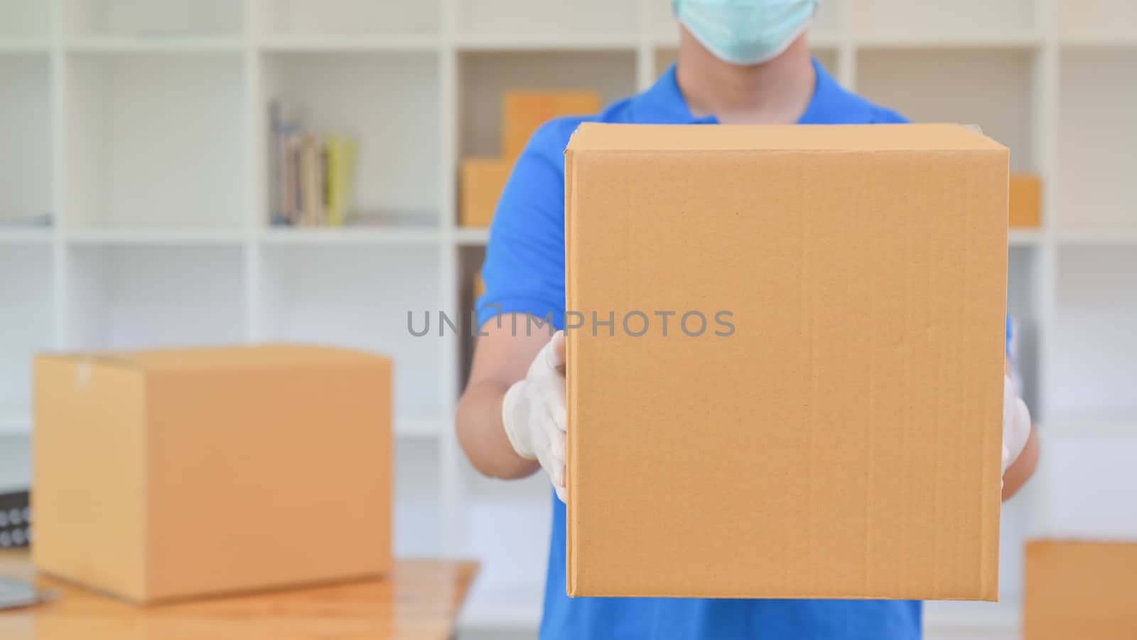 The delivery staff held a brown paper box. He was wearing gloves and a mask.