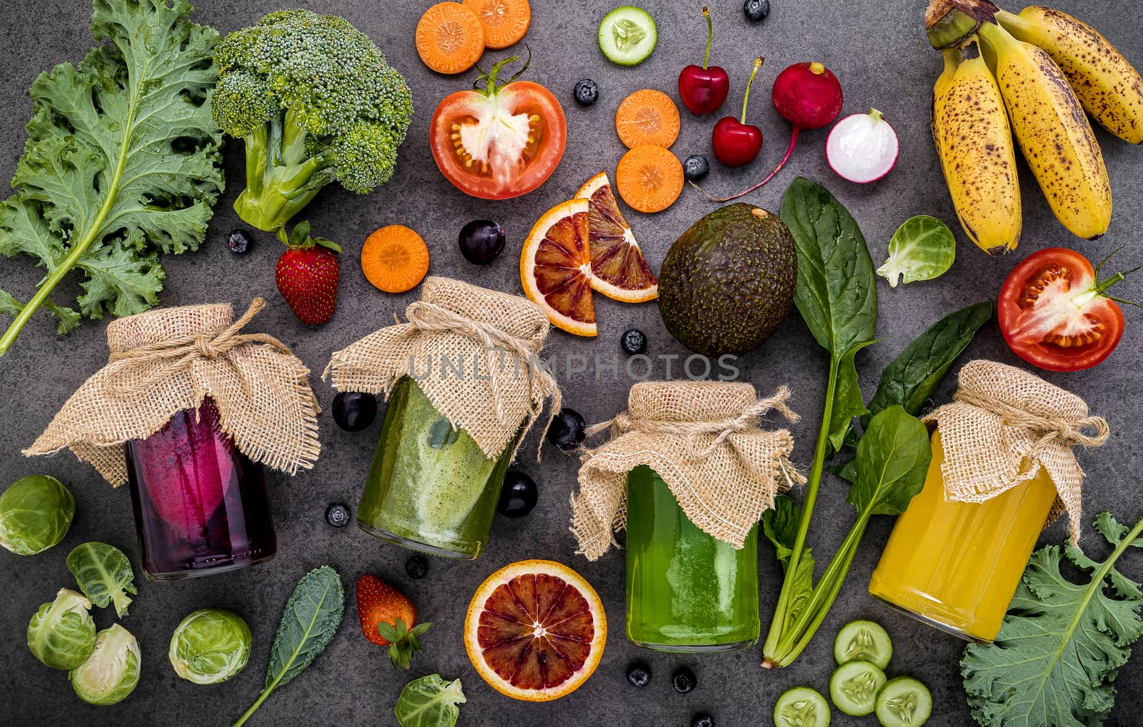 Colourful healthy smoothies and juices in bottles with fresh tropical fruit and superfoods on dark stone background with copy space.