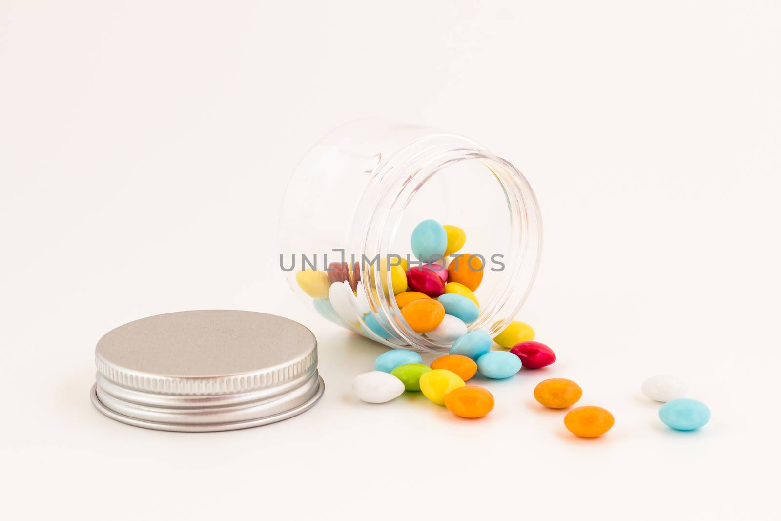Colored smarties scattered out of an open glass jar, isolated on white background. Shallow depth of field.