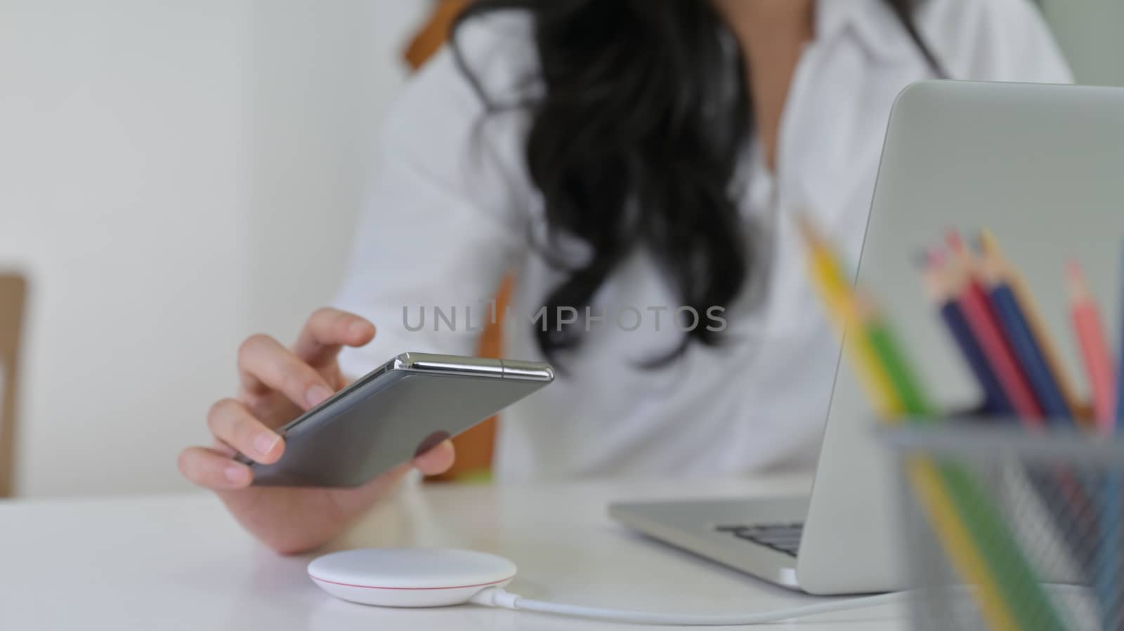 Close-up shot of Girl are putting the smartphone on wireless charger with laptop on the desk.