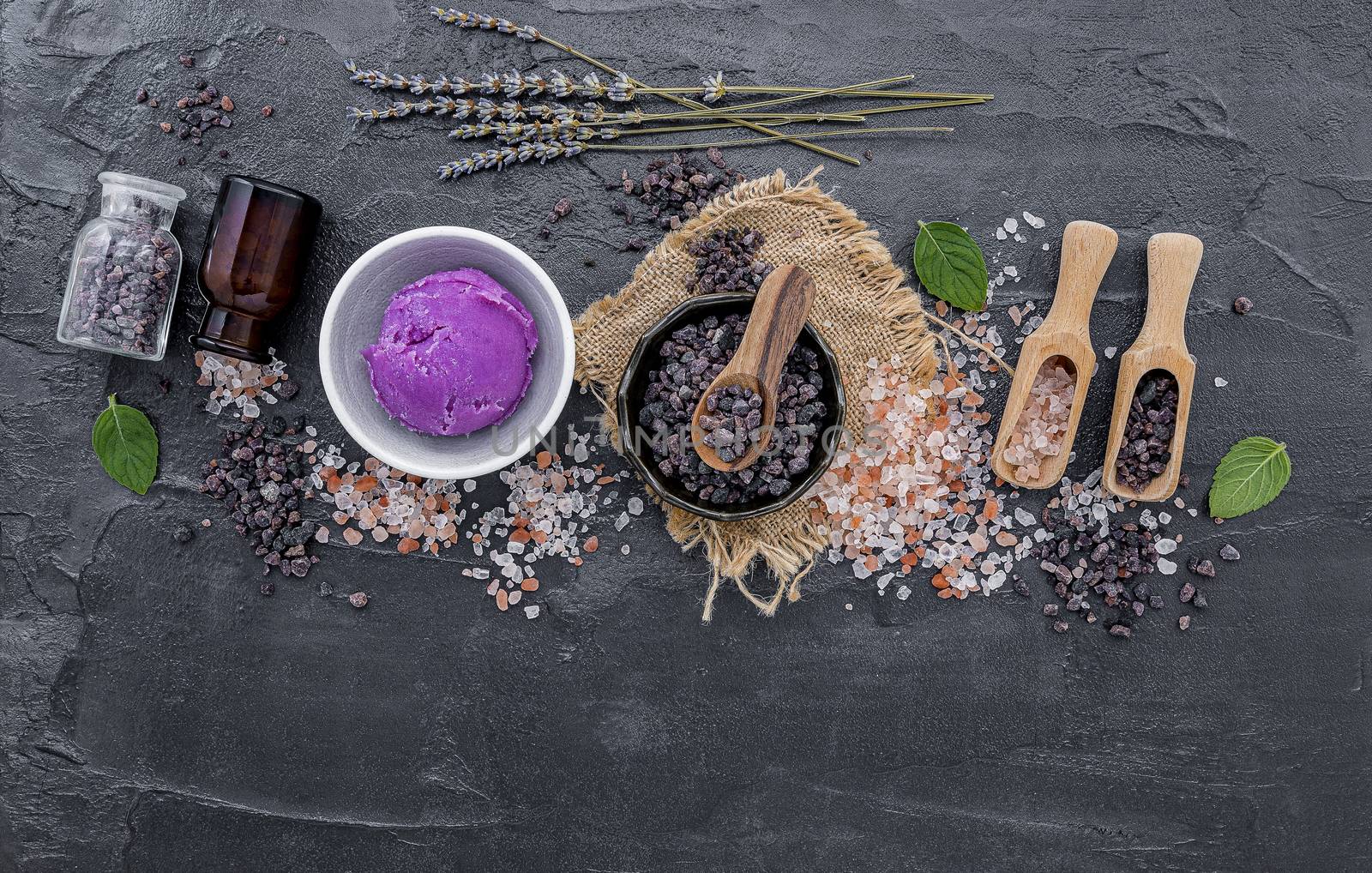 Himalayan black salt and Himalayan pink salt with peppermint and lavender flower on dark concrete background. Himalayan salt commonly used in cooking and for bath products such as bath salts.