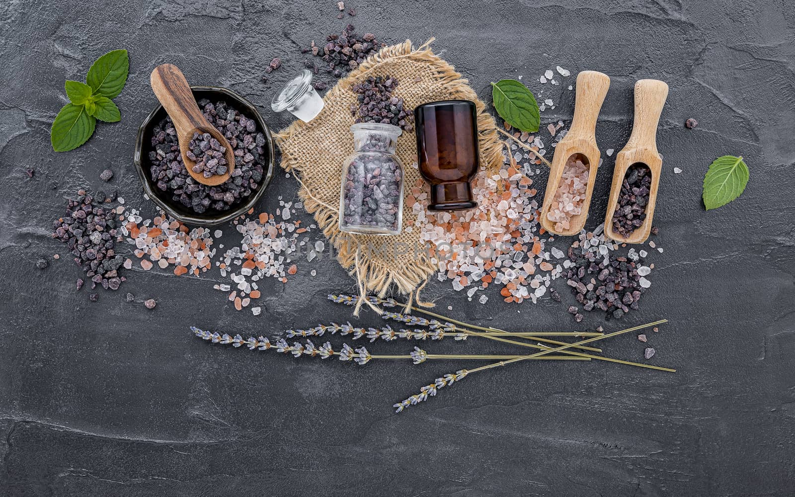 Himalayan black salt and Himalayan pink salt with peppermint and lavender flower on dark concrete background. Himalayan salt commonly used in cooking and for bath products such as bath salts.