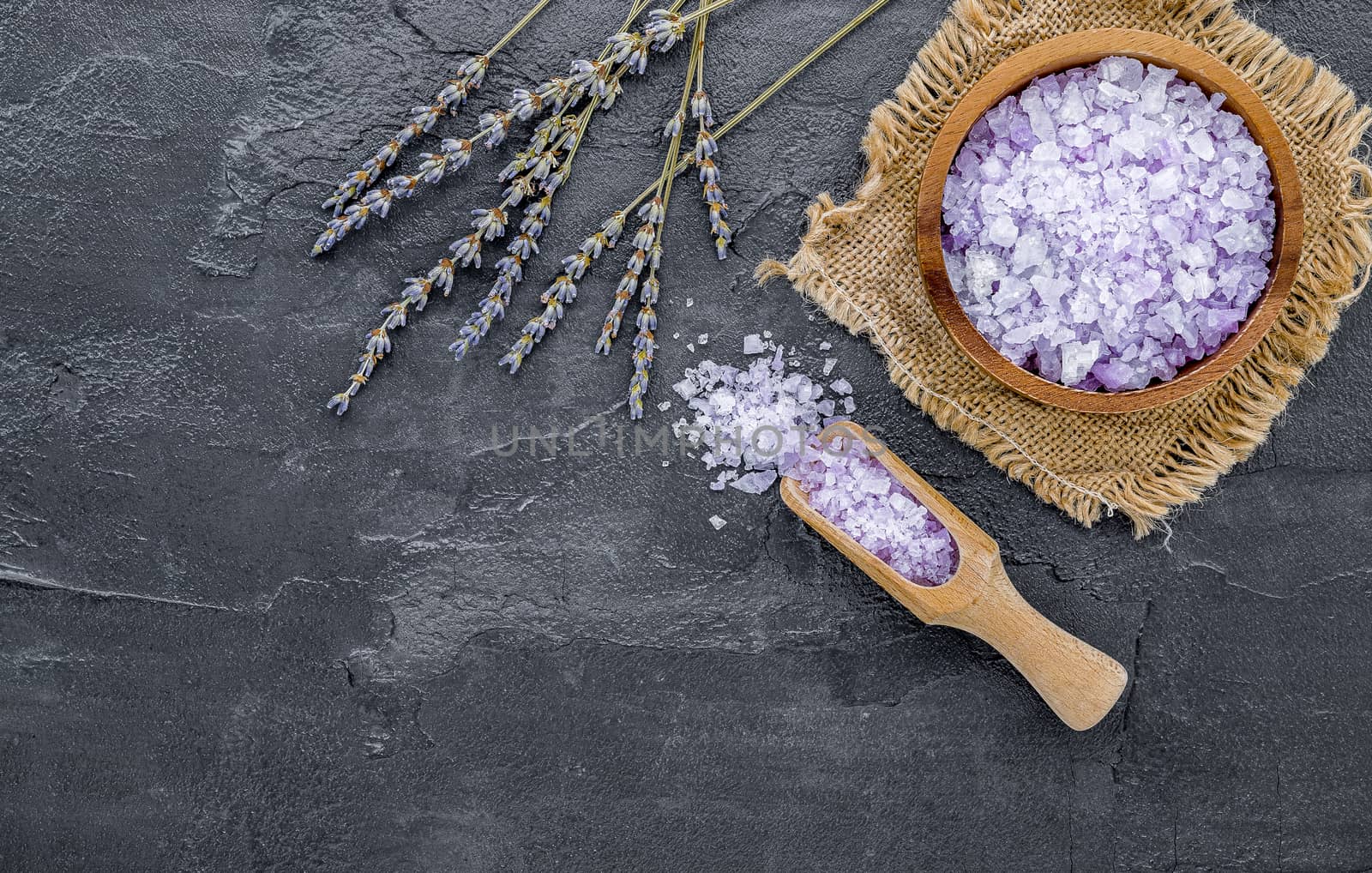 Aromatic purple bath salt with lavender flower on dark concrete background. Himalayan salt commonly used in cooking and for bath products such as bath salts.