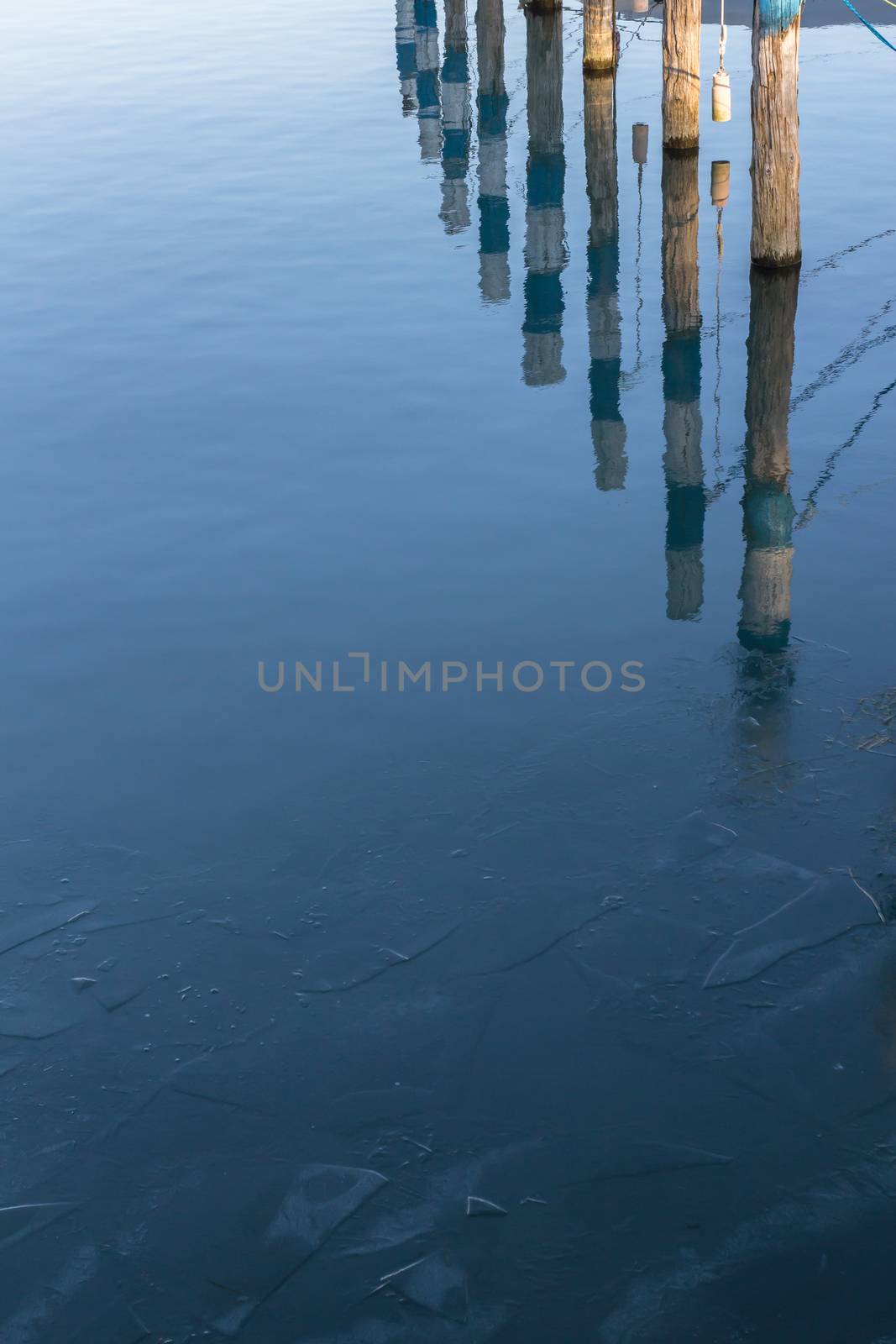 Wooden piers reflexes on the surface of the frozen lake
