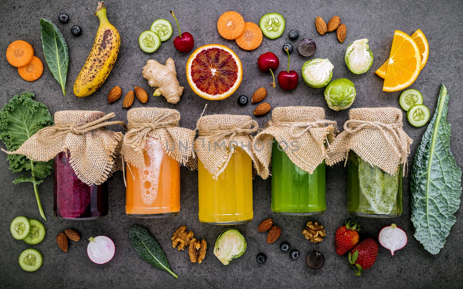 Colourful healthy smoothies and juices in bottles with fresh tropical fruit and superfoods on dark stone background with copy space.