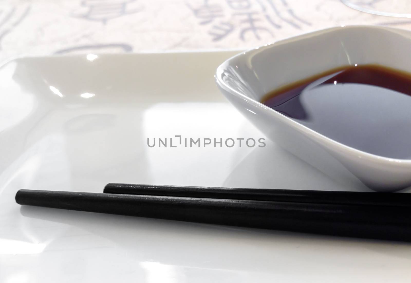 Soy sauce dish with a couple of chopsticks. Shallow depth of field. Defocused blurry background.