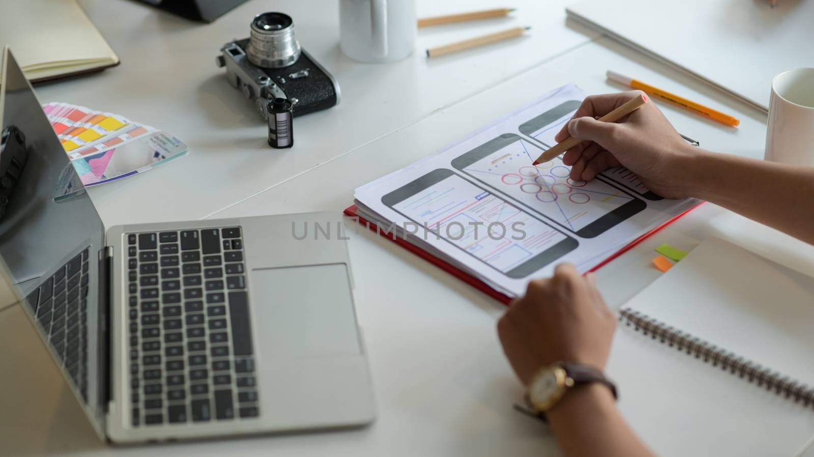 Cropped shot of Designer is sketching a smartphone screen for future customers on the desk with laptop and stationeries.