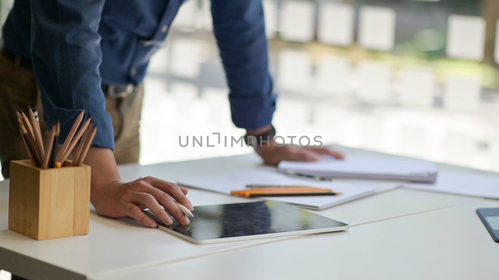 Young man holding a pen to use a tablet on the desk with station by poungsaed