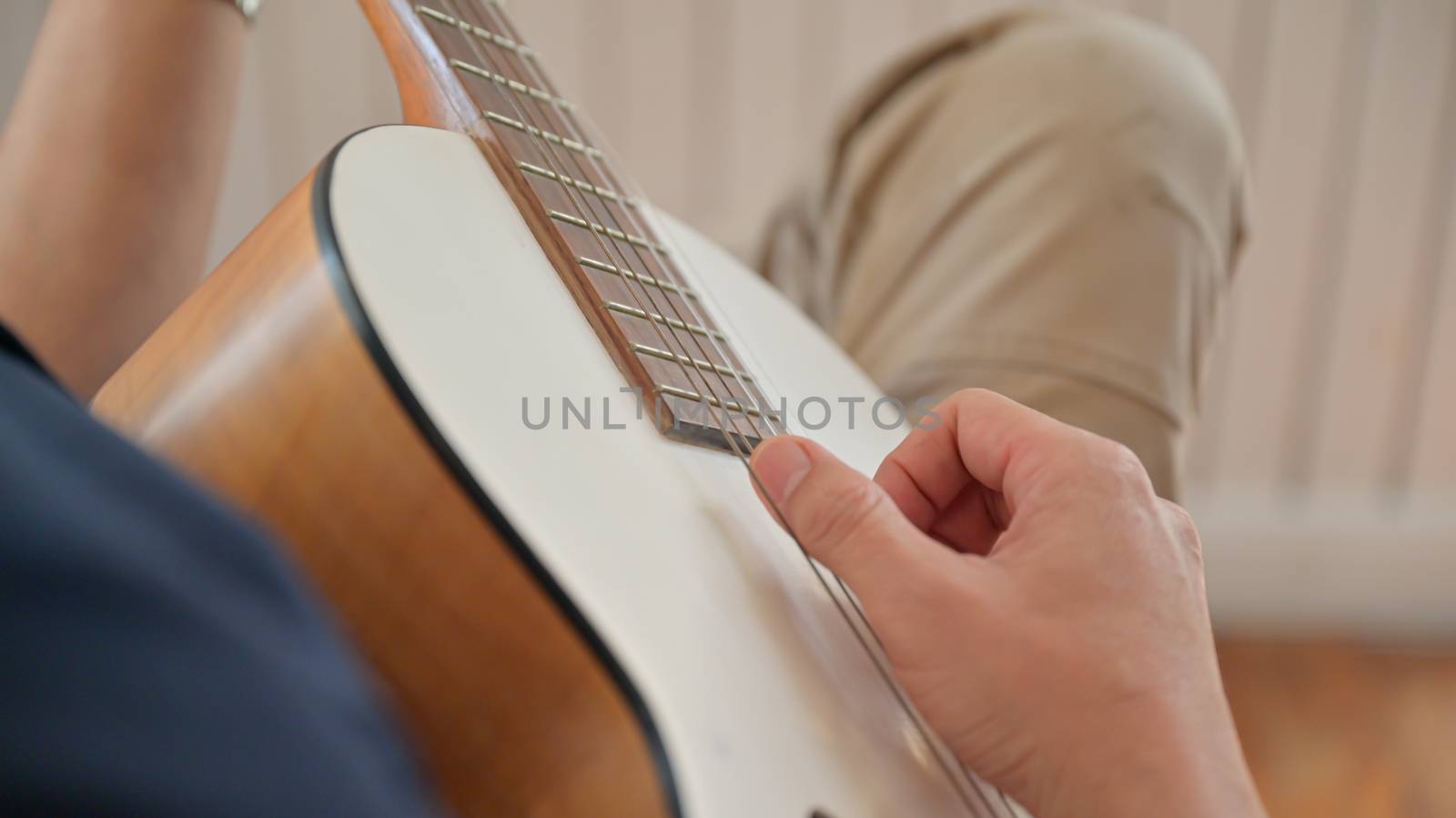 Close-up shot of a young man playing guitar at home He stopped at home because of the virus outbreak,shot from above the shoulder.