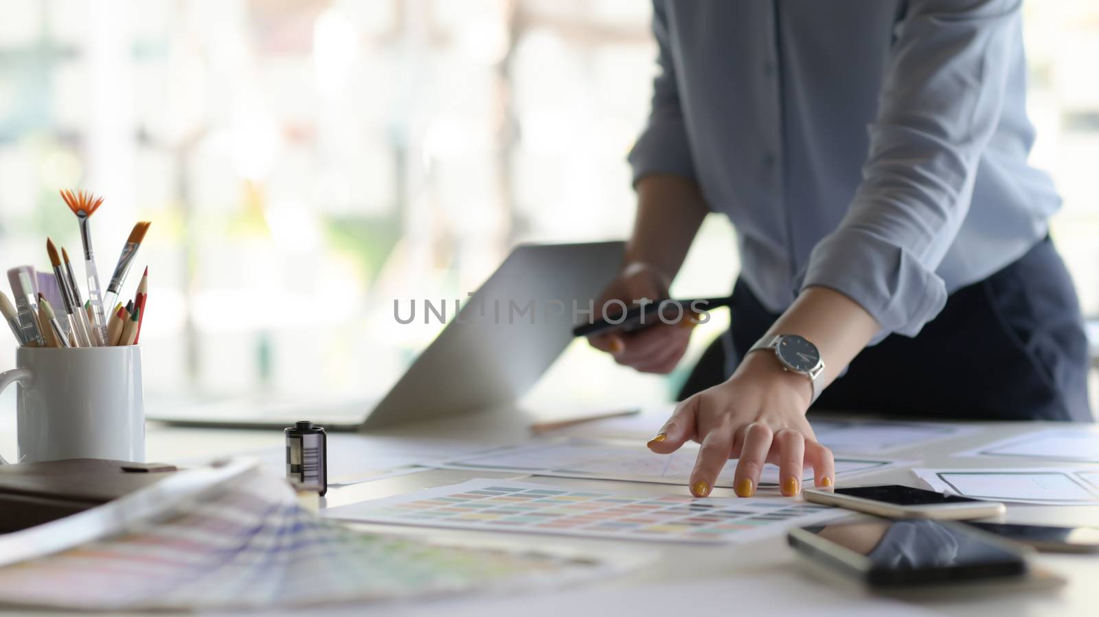 Cropped shot of young designer working on new application project while using smartphone in modern office room.