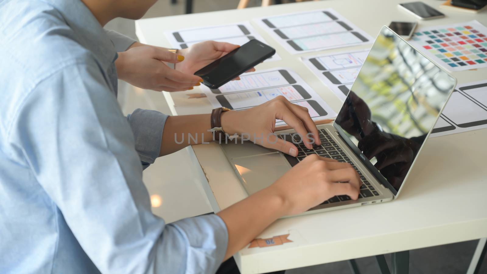 The UX team is designing an application for smartphones with a laptop in a modern office.