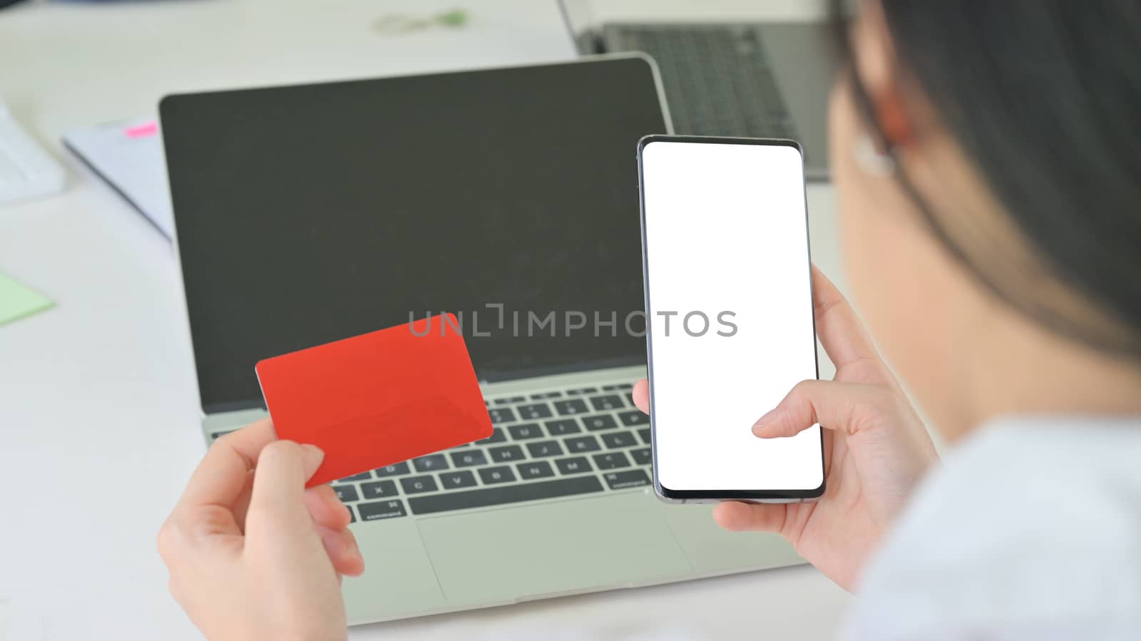 Close - up shot of Credit card and smartphone in the woman hand and the laptop on the back.
