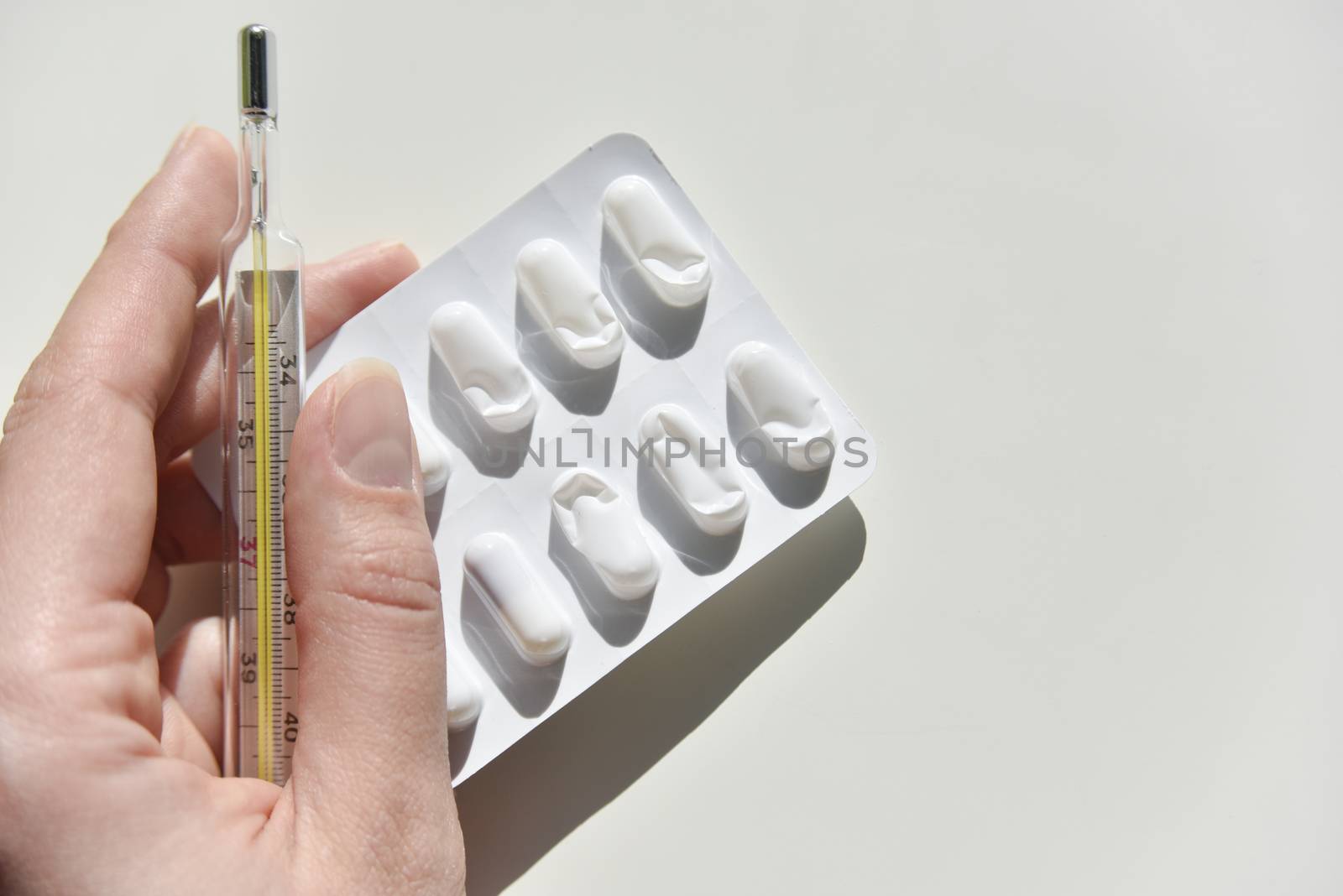 thermometer and pack of pills on the white background with the humans hand 