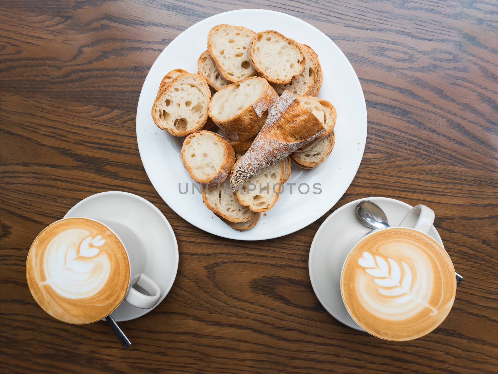 Two cappuccino cups and sliced bread on a wooden table