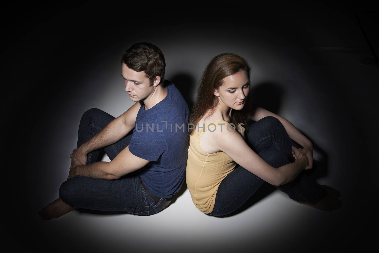 Unhappy Young Couple Sitting In Pool Of Light