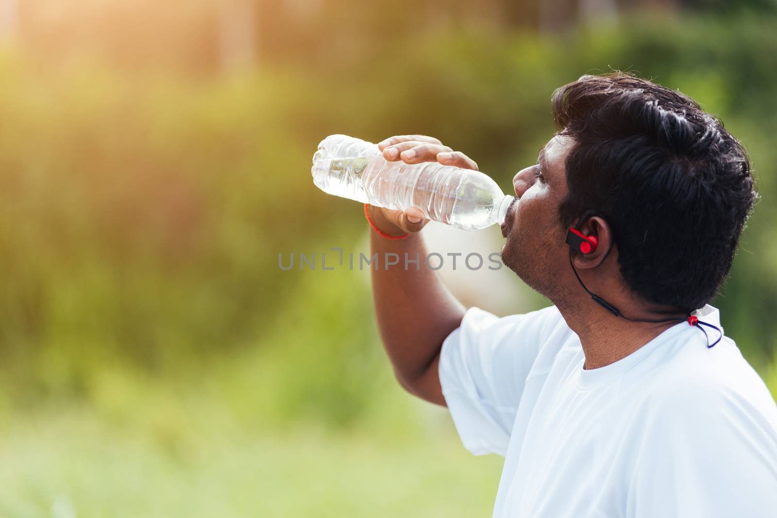 Close up Asian young sport runner black man wear athlete headphones he drinking water from a bottle after running at the outdoor street health park, healthy exercise workout concept