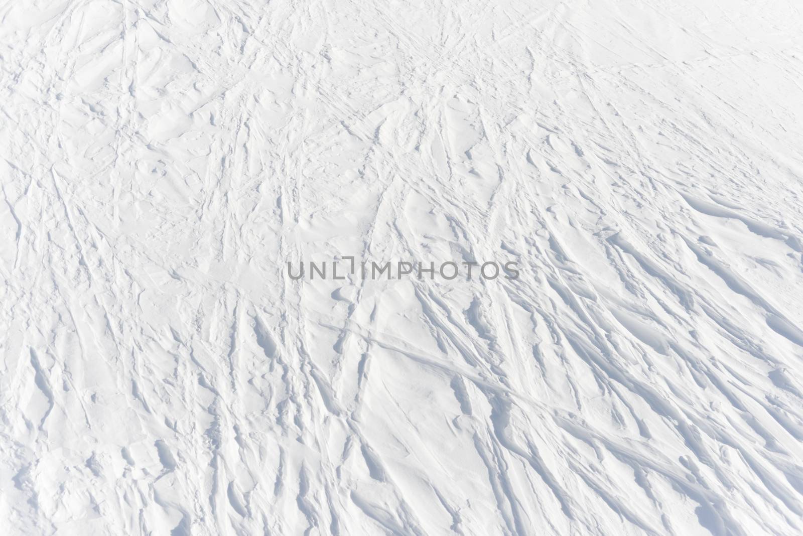 3 - gently curving linear tracks left from absent skiers cross into an intricate lattice pattern in the pure white alpine snow, background texture