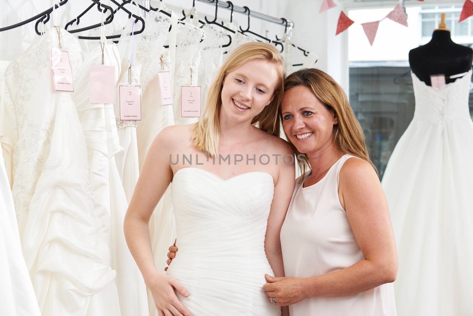 Mother Helping Daughter To Choose Dress In Bridal Store