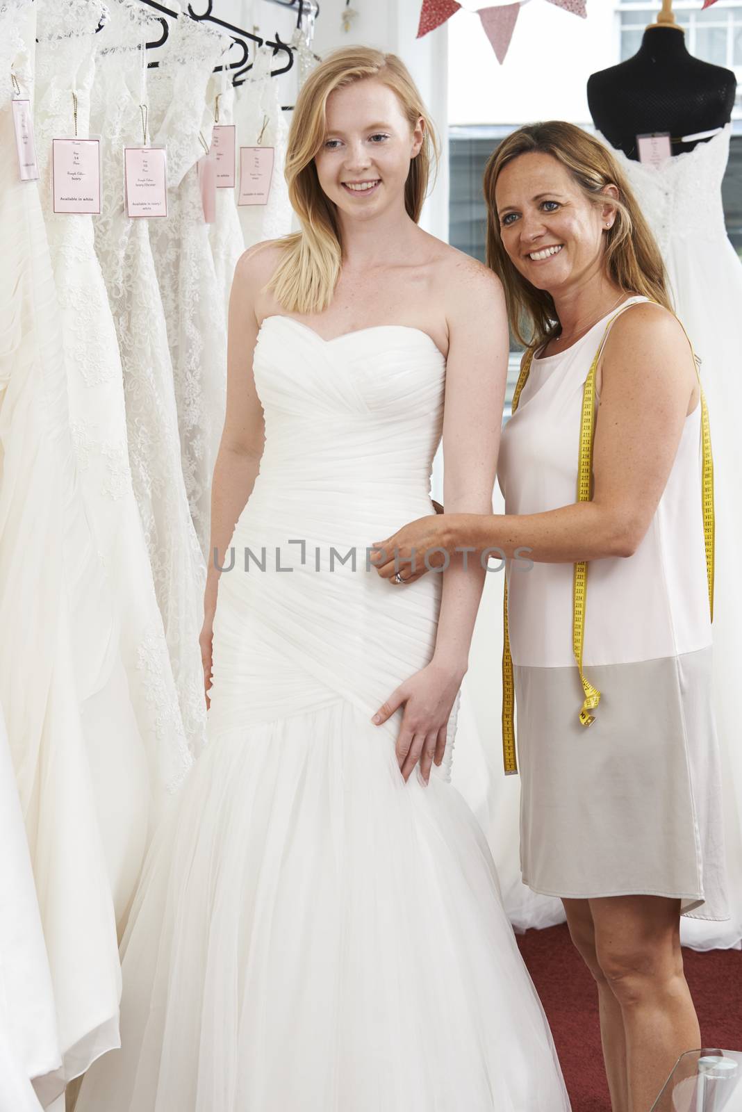 Bride Being Fitted For Wedding Dress By Store Owner
