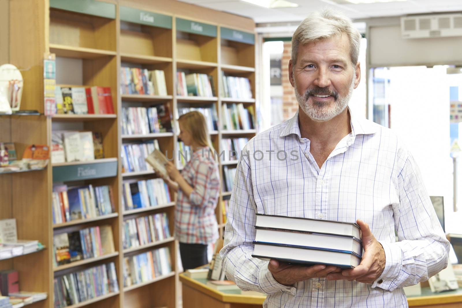 Portrait Of Male Bookstore Owner With Customer In Background by HWS