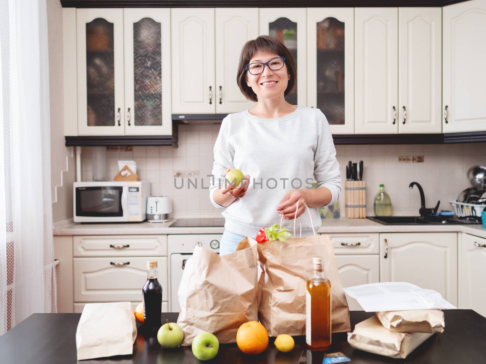 Woman sorts out purchases in the kitchen. Grocery delivery in paper bags. Subscription service from grocery store in conditions of quarantine because of coronavirus COVID19.