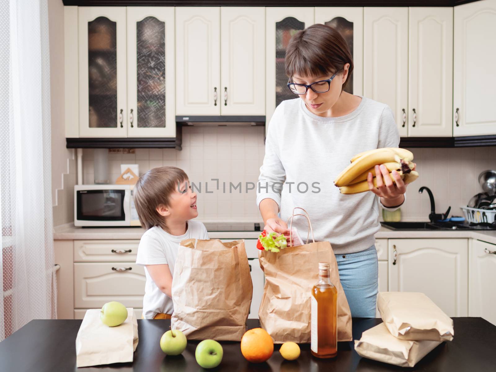 Woman and toddler boy sorts out purchases in the kitchen. Kid bi by aksenovko