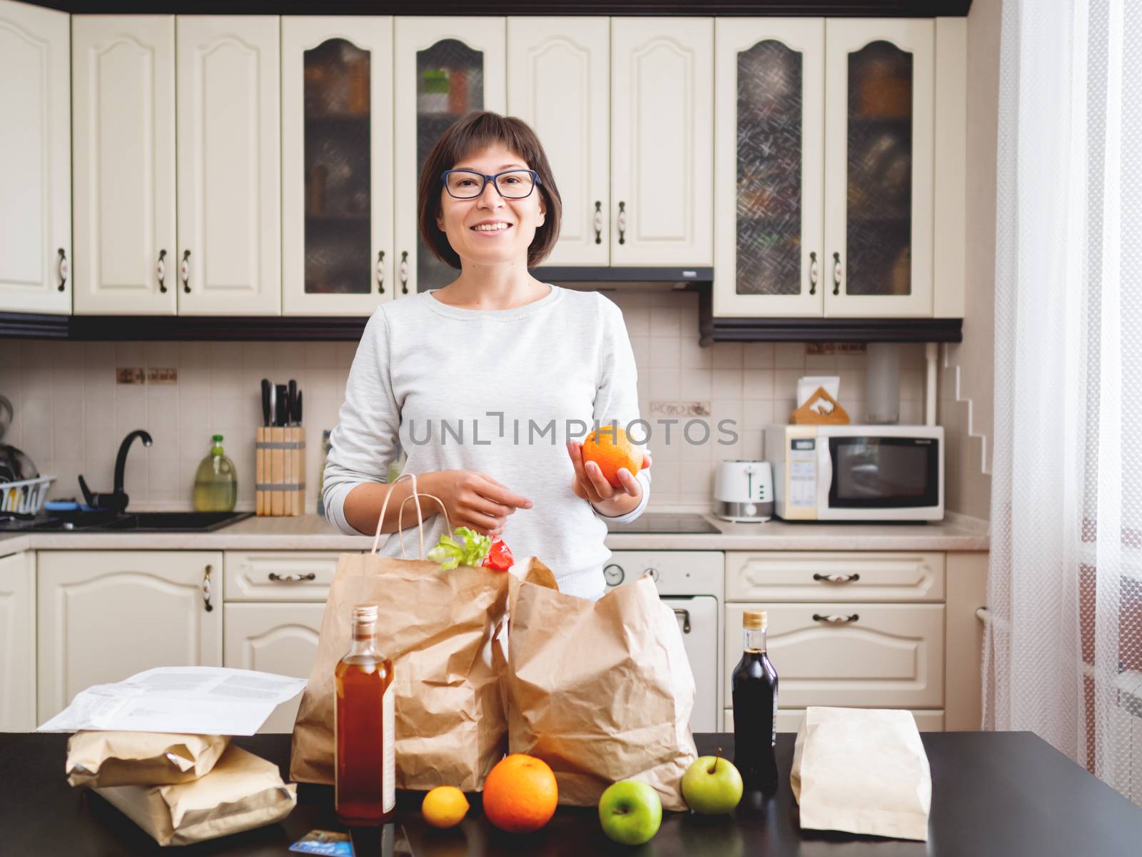 Woman sorts out purchases in the kitchen. Grocery delivery in paper bags. Subscription service from grocery store in conditions of quarantine because of coronavirus COVID19.