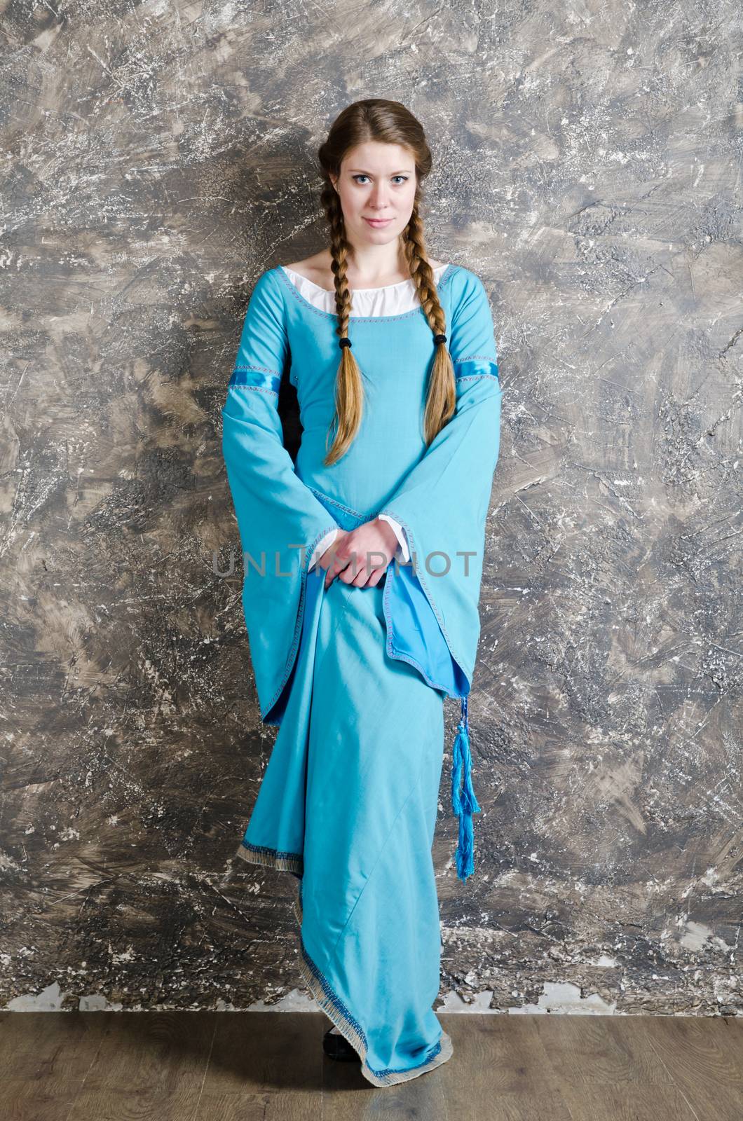 Pretty young woman in historical medieval blue dress poses in studio