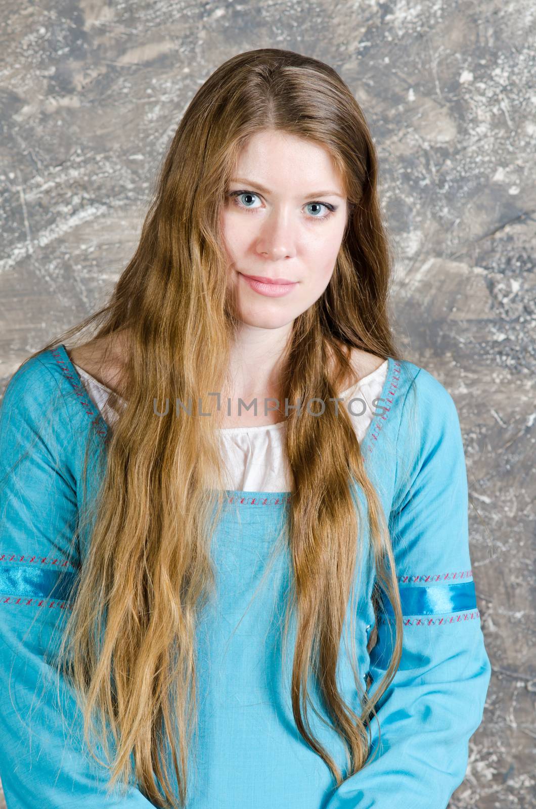 Pretty young woman in historical medieval blue dress poses in studio