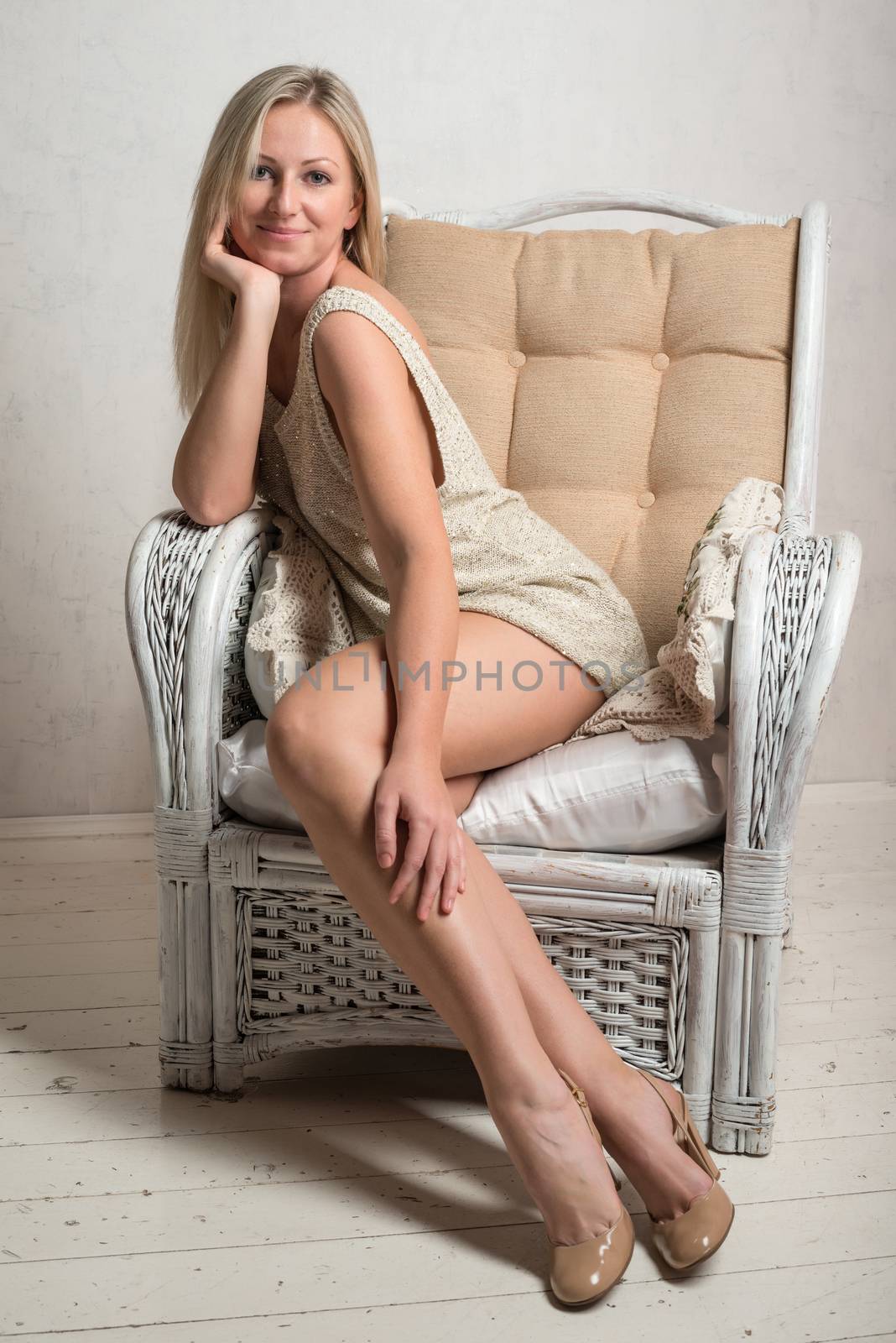 Smiling beautiful attractive woman in short dress is posing in a retro armchair