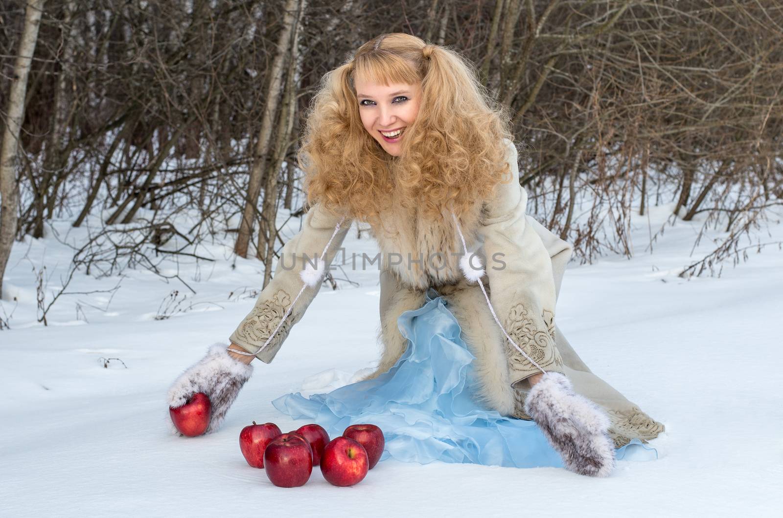 Smiling young woman with unusual hairstyle poses with apples in winter forest