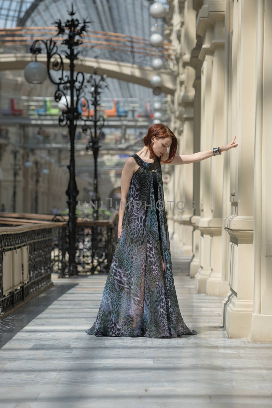 Caucasian tender young model is posing in a short black dress and lengthy transparent cape at old fashioned building with pillars