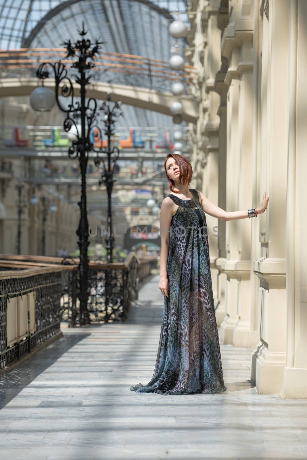 Caucasian tender young model is posing in a short black dress and lengthy transparent cape at old fashioned building with pillars