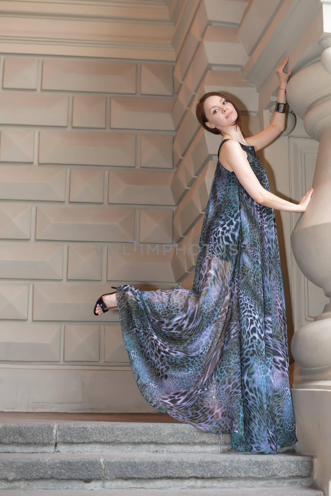 Charming lovely woman in gorgeous dress is posing on stairs of historic building