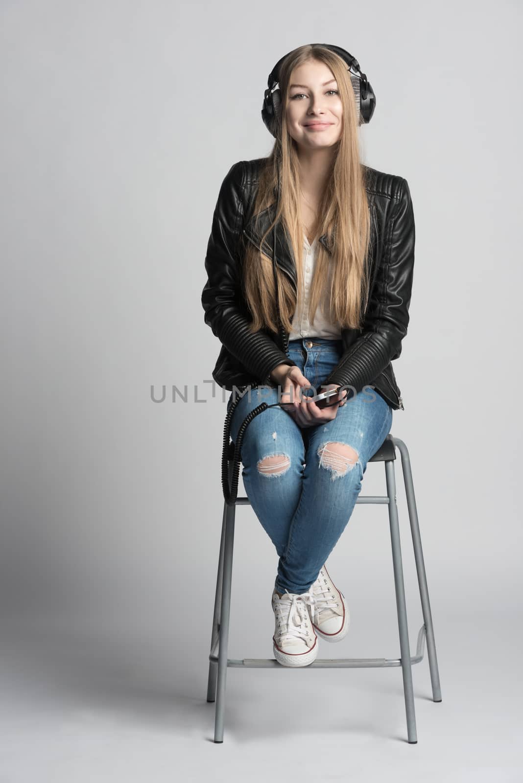 Adorable smiling girl in wired headphones is sitting and listening music from her own phone